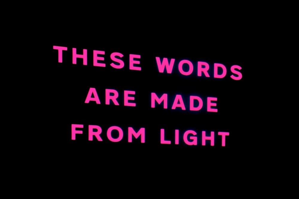 Bright pink text against a black background reads, "THESE WORDS ARE MADE FROM LIGHT."