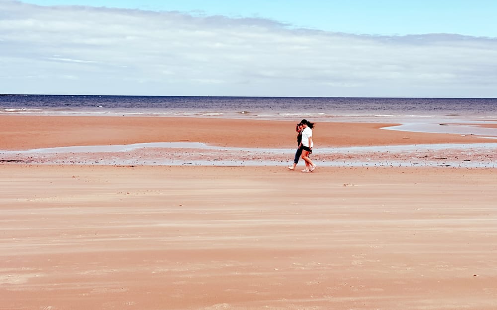 Two people walking on an expansive beach with blue skies and the Moray Firth in the background