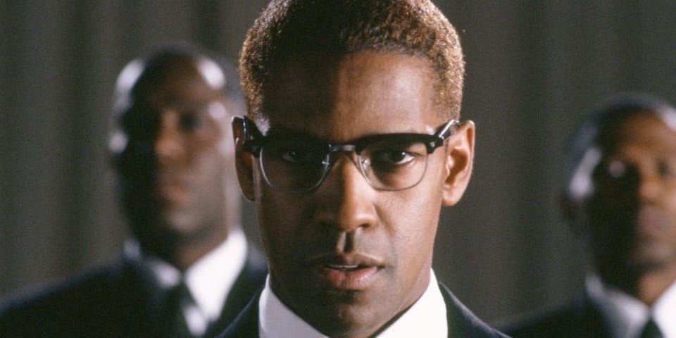 Denzel Washingto as Mallcolm X staring down the barrel of the camera. Flanked either side by other men.